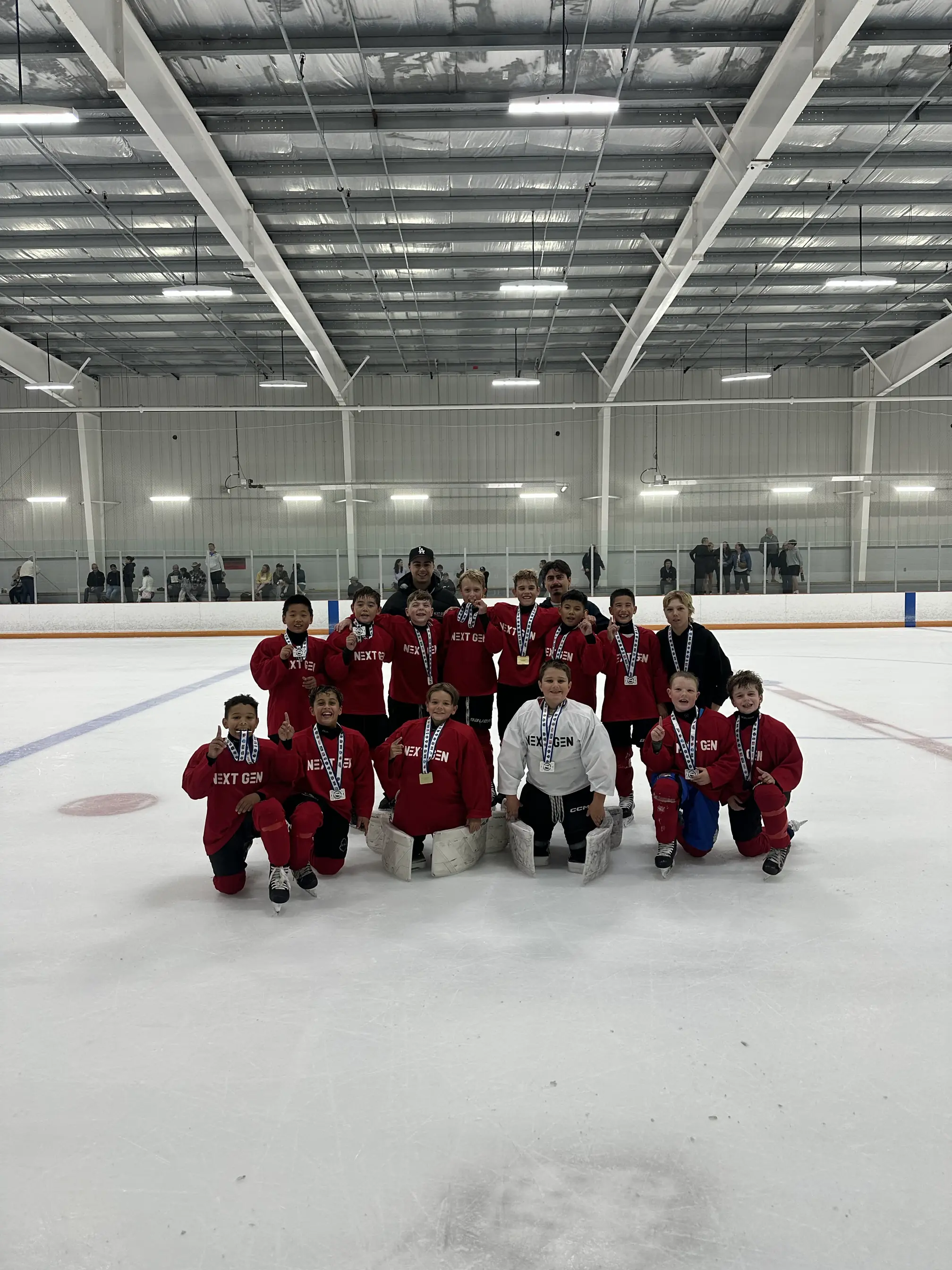 The NextGen Hockey School squad on the ice in red NEXT GEN jerseys, wearing medals, with their coach standing behind them